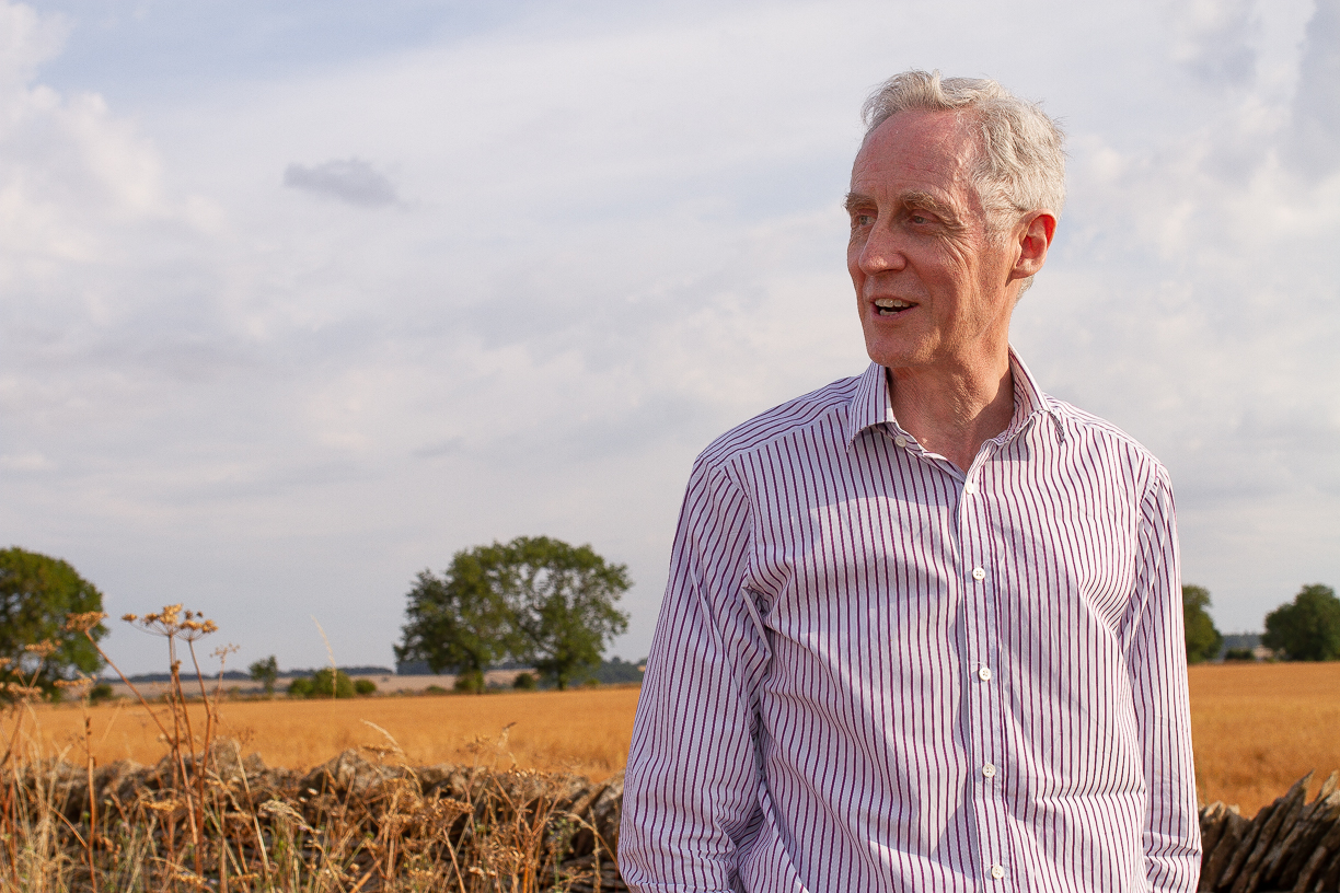 Man standing, looking to his right in front of wheat field and trees