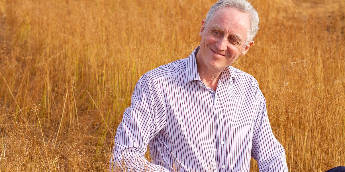 Coach sitting in a grassy sunlit field, smiling and looking to his right