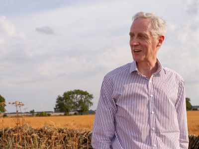 Man standing, looking to his right in front of wheat field and trees