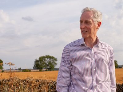Man standing, looking to his right in front of wheat field and trees